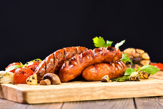 Grilled sausages and various vegetables on chopping wood