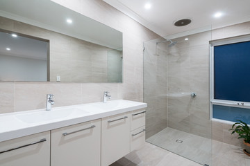 Modern stylish bathroom interior with floor to ceiling tiling, glass screen, and large mirror.