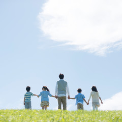 草原で手をつなぐ小学生と先生の後姿