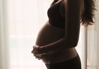 Pregnant woman standing by the window at home.