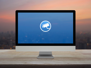 cctv camera flat icon on desktop modern computer monitor screen on wooden table over blur of cityscape on warm light sundown, Business security and safety online concept