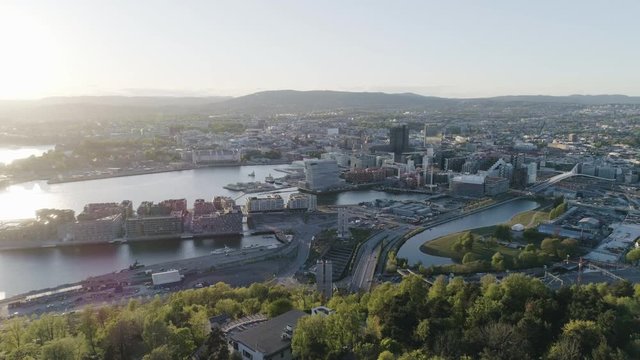 4K aerial of the Oslo city line with a backdrop of Oslo and Bjoervika, a popular tourist attraction with the Munch museum, Barcode, Opera and Soerenga pier, in a sunset with backward motion.