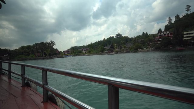 Footage from a ferry traveling across Lake Toba in North Sumatra, Indonesia, passing traditional Batak-style lake-side resorts.
