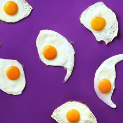 Fried eggs or scrambled eggs pattern on violet background. Creative food concept. Top view. Square crop
