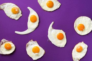 Fried eggs or scrambled eggs pattern on violet background. Creative food concept. Top view. Minimalistic style