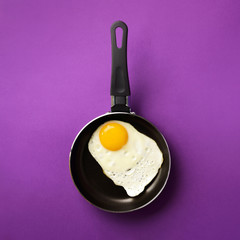 Creative food concept with fried egg on pan over violet background. Top view. Creative pattern in minimal style. Flat lay. Square crop
