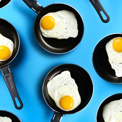 Creative food pattern with fried eggs on pans over blue background. Top view. Creative pattern in...