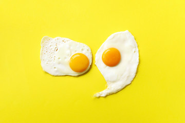 Two fried eggs on yellow paper background. Creative food concept in minimal style. Top view