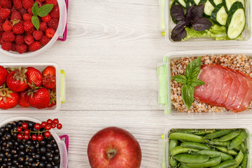 Apple and plastic meal prep containers with fresh berries, boiled buckwheat porridge and slices of meat, cucumbers and salad.