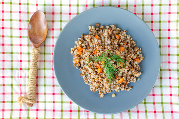 Buckwheat porridge in a gray plate on a background of a checkered napkin. Healthy food.