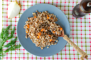 Buckwheat porridge in a gray plate on a background of a checkered napkin. Healthy food.