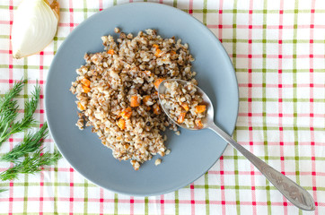 Buckwheat porridge in a gray plate on a background of a checkered napkin. Healthy food.