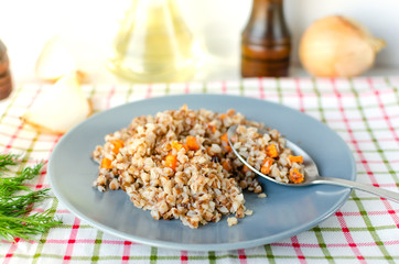 Buckwheat porridge in a gray plate on a background of a checkered napkin. Healthy food.