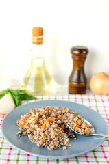 Buckwheat porridge with carrots and dill in gray plate. On the background of Golden onions, green parsley and salt and pepper mills.
