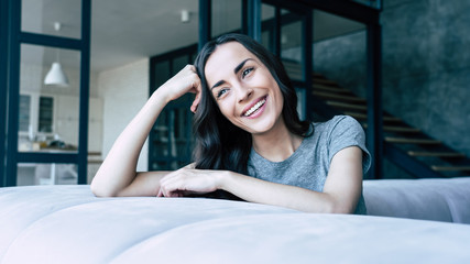 Close up photo of smiling beautiful woman relaxing at home while sitting on the couch and looks away