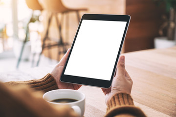 Mockup image of a woman holding black tablet pc with blank white screen with coffee cup on wooden table