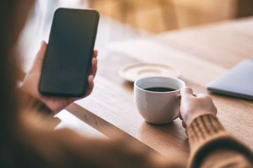 Closeup image of a woman holding and using smart phone while drinking coffee on wooden table