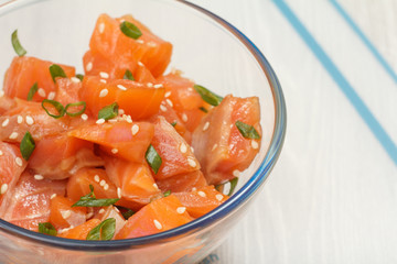 Hawaiian salmon poke with green onions and sesame seeds in glass bowl.