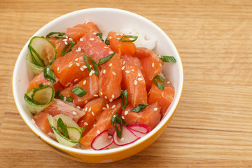 Hawaiian poke with salmon and sesame seeds, boiled rice, fresh cucumber, radish and green onions in glass bowl.