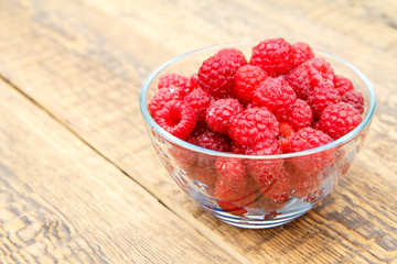 Ripe raspberries in the glass bowl on wooden boards.