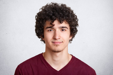 Close up portrait of curly handsome European male, wearing casual maroon shirt, isolated over white...