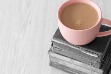 Cup of tea in a pink cup on a stack of old antique books with selective colour on a grey wood background