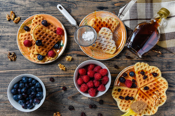 A top view image of belgian gaufre with maple syrup and forest fruits on rustic wooden table