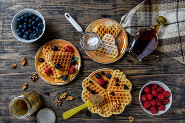A top view image of belgian gaufre with maple syrup and forest fruits on rustic wooden table