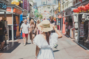 Young Woman traveling with white dress and hat, happy Asian traveler walking at Chinatown street market in Singapore. landmark and popular for tourist attractions. Southeast Asia Travel concept