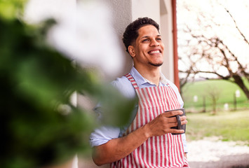 A portrait of young man gardener outdoors at home, holding a cup of coffee.