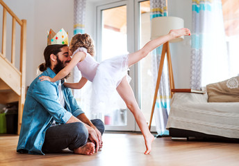 Side view of small girl with a princess crown and young father at home, playing.