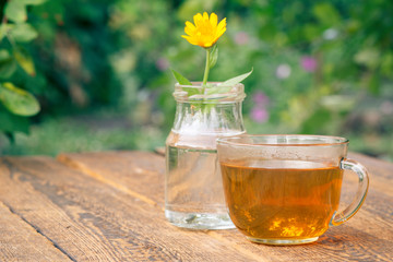Cup of green tea and calendula flower with a stem in a glass flask.