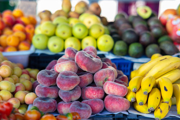 A fruit stall on a Spanish weekly market with peaches, plums, avocados, bananas, apples and other fruits. Everything is very fresh and colorful in sunny weather.