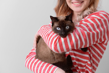 Young woman with cute Thai cat on light background