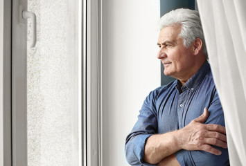 Portrait of handsome senior man near window at home