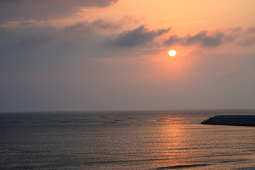 Fototapeta premium Seascape at Yellow glowing sun setting in the horizon with breakwater.