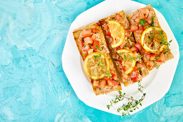 Appetizer bruschetta with tuna and tomatoes in white plate on blue background. Italian cuisine. Delicious Italian antipasti crostini. Copy space. Top view.