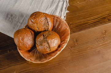 Craft three bread buns in a wicker basket, on a wooden cutting board. Simple breakfast on wooden background. copy space.