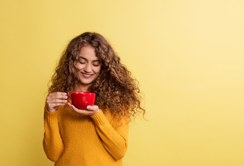 Portrait of a young woman with red cup in a studio on a yellow background.