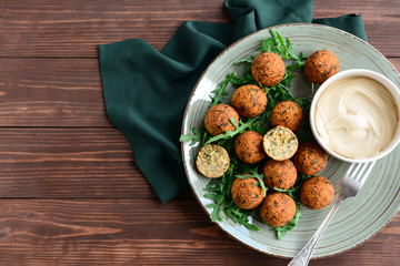 Plate with tasty falafel balls and sauce on wooden table
