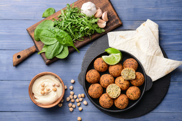 Frying pan with tasty falafel balls and sauce on wooden table