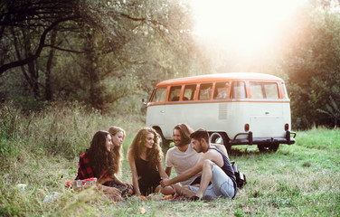 A group of friends sitting on ground on a roadtrip through countryside, having picnic.