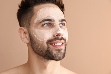 Handsome man with clay mask on his face against color background