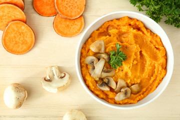 Bowl with mashed sweet potato and mushrooms on wooden background