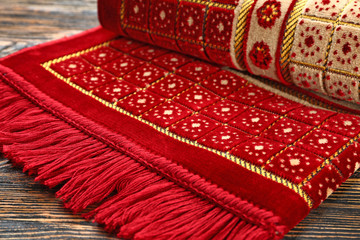 Muslim prayer rug on wooden background, closeup