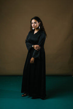 Studio portrait of a beautiful and attractive Malay Asian woman in a traditional black baju kurung dress against a brown background. She has frizzy beautiful hair and is posing for her portrait. 