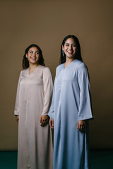 Portrait of two young Middle Eastern Muslim women smiling as they pose for their photo. They are wearing traditional pastel coloured Baju Kurung dresses to visit during Raya. 