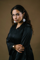 Studio portrait of a beautiful and attractive Malay Asian woman in a traditional black baju kurung dress against a brown background. She has frizzy beautiful hair and is posing for her portrait