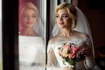 Portrait of a blonde bride with a bouquet of roses indoor.Pretty happy bride in luxury dress near...