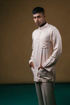 Studio Portrait Of A Young, Handsome And Athletic Malaysian Indian Muslim Asian Man In A Cream Colored Traditional Baju Melayu Tunic. He Is Dressed Festively To Go Visiting For Raya. 